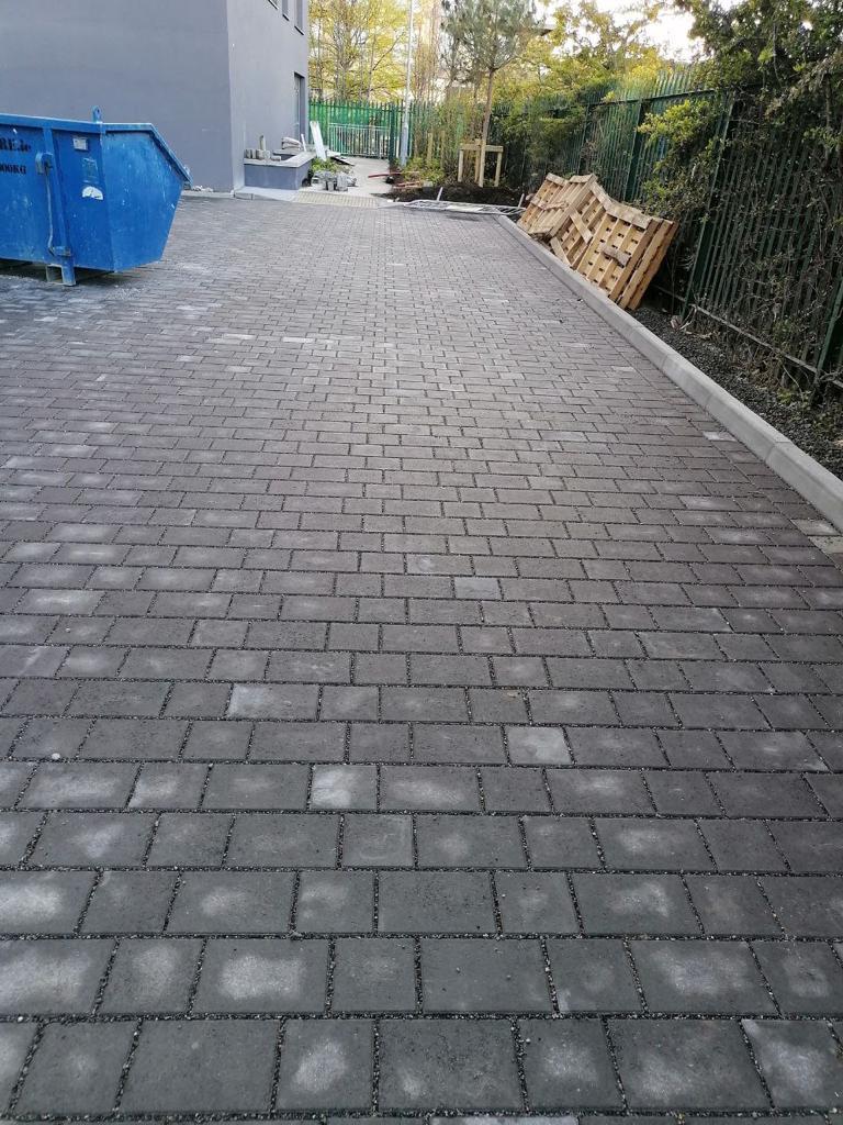 A brick pavement under construction with a blue skip and a metal fence